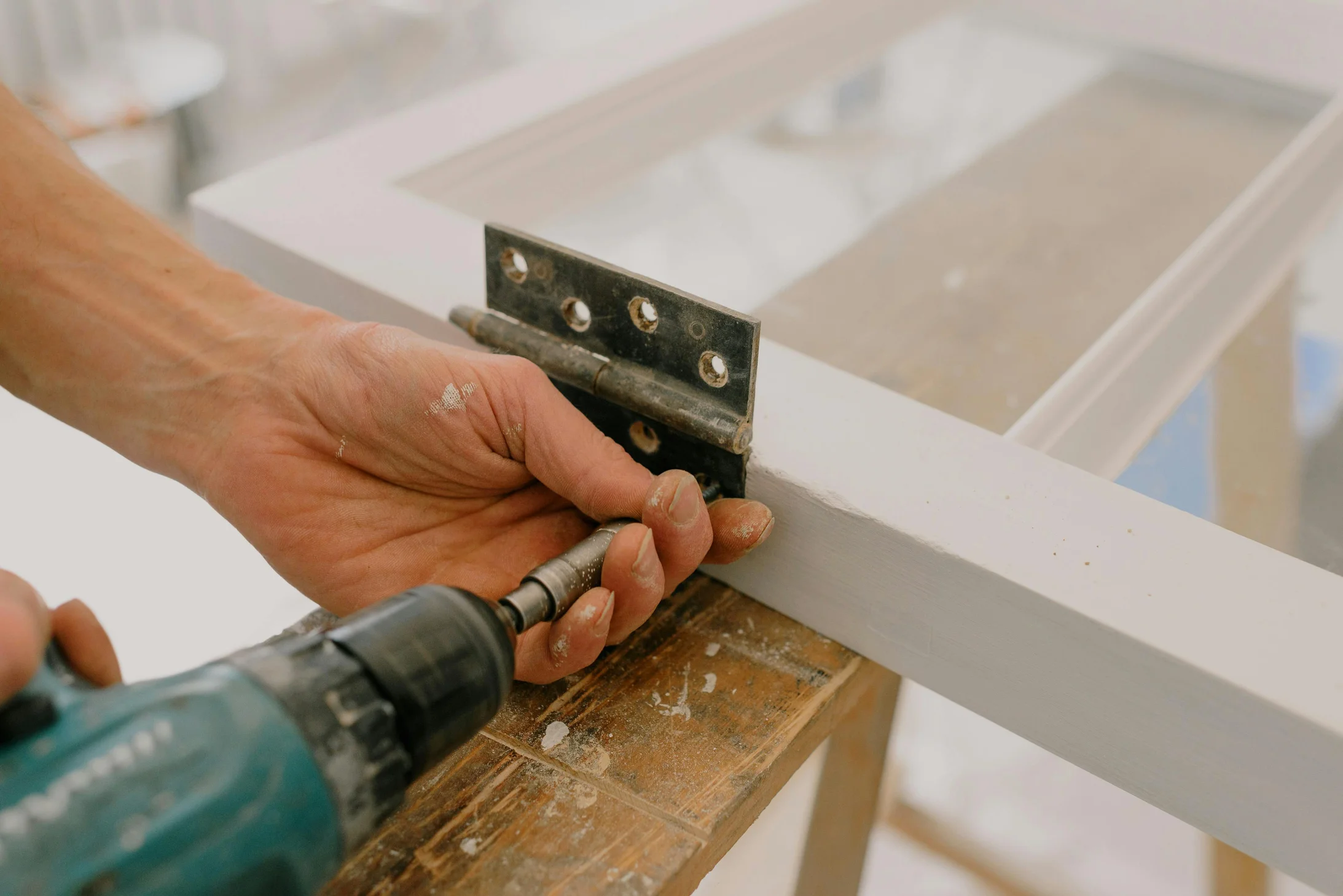 Handwerker bohrt Scharnier an Fensterrahmen