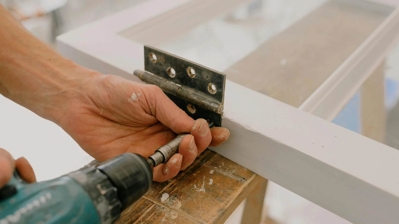 Handwerker bohrt Scharnier an Fensterrahmen